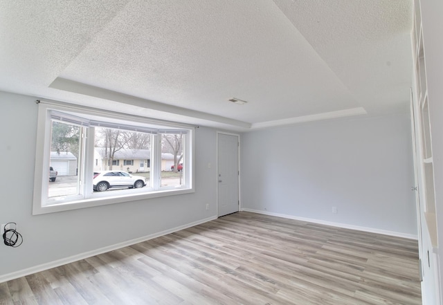 empty room featuring a tray ceiling, baseboards, a textured ceiling, and wood finished floors