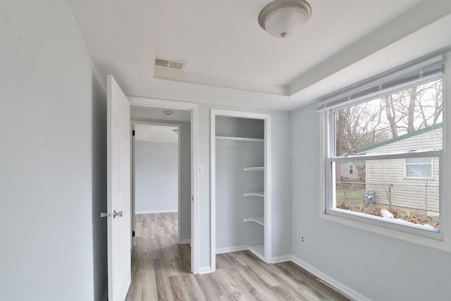 unfurnished bedroom with visible vents, baseboards, light wood finished floors, a tray ceiling, and a closet