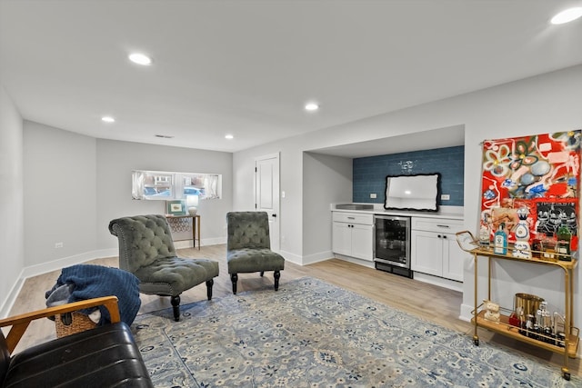 living room with beverage cooler, baseboards, light wood finished floors, recessed lighting, and a bar