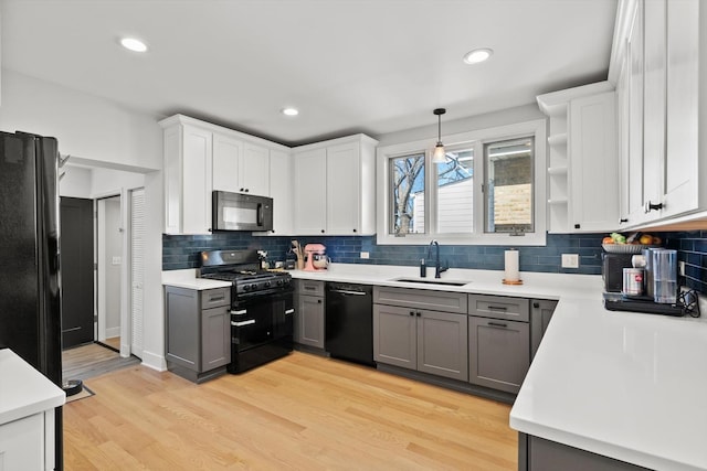 kitchen featuring light wood finished floors, light countertops, gray cabinets, black appliances, and a sink