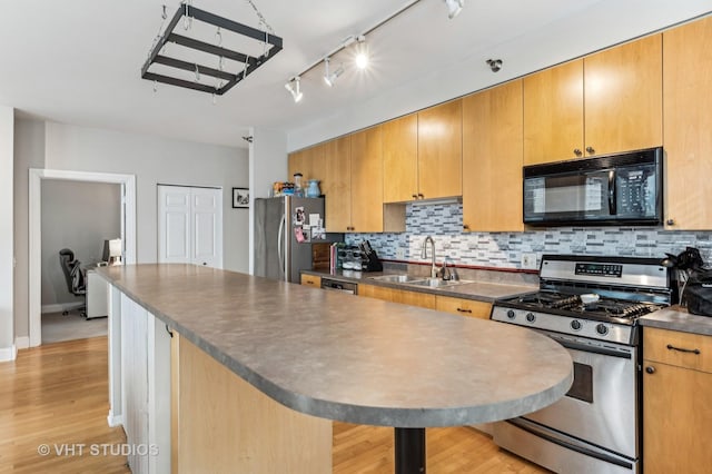 kitchen with dark countertops, decorative backsplash, light wood-style floors, stainless steel appliances, and a sink