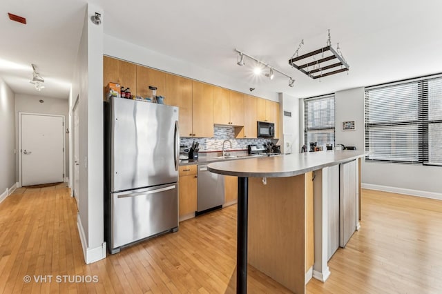 kitchen featuring a sink, a kitchen island, appliances with stainless steel finishes, light wood finished floors, and decorative backsplash