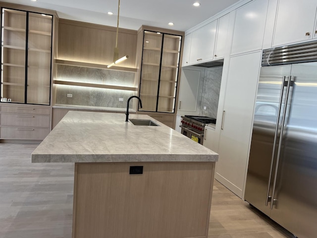 kitchen featuring light wood-type flooring, premium appliances, recessed lighting, decorative backsplash, and a sink