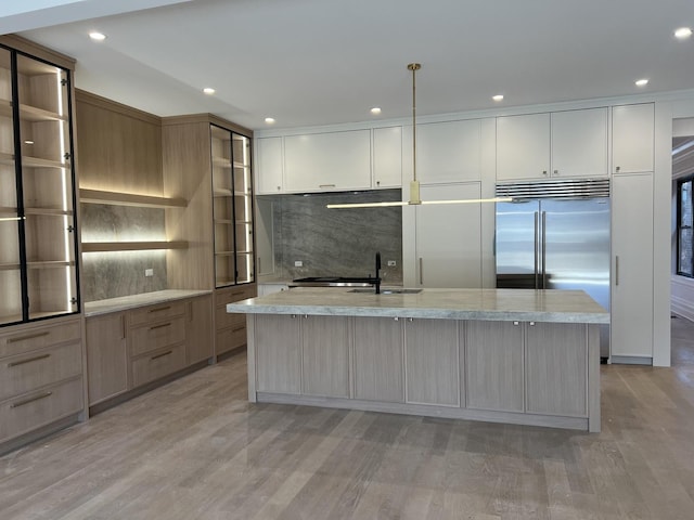 kitchen with recessed lighting, a kitchen island with sink, stainless steel built in fridge, light wood-style floors, and tasteful backsplash