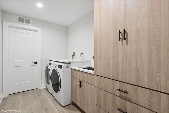 laundry room featuring visible vents, a sink, washing machine and dryer, cabinet space, and light wood finished floors