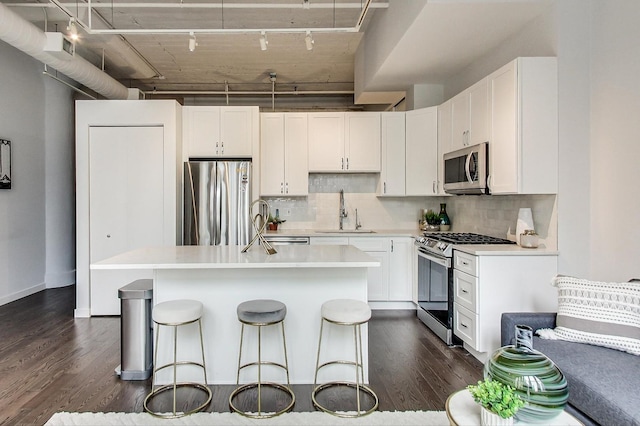 kitchen with a center island with sink, a sink, dark wood-style floors, stainless steel appliances, and white cabinets