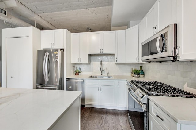 kitchen with dark wood finished floors, a sink, appliances with stainless steel finishes, white cabinetry, and tasteful backsplash