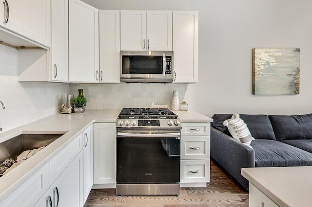 kitchen with light wood finished floors, backsplash, appliances with stainless steel finishes, and white cabinetry