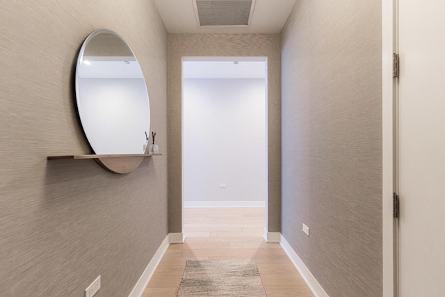 hall with visible vents, baseboards, light wood-style flooring, and a textured wall