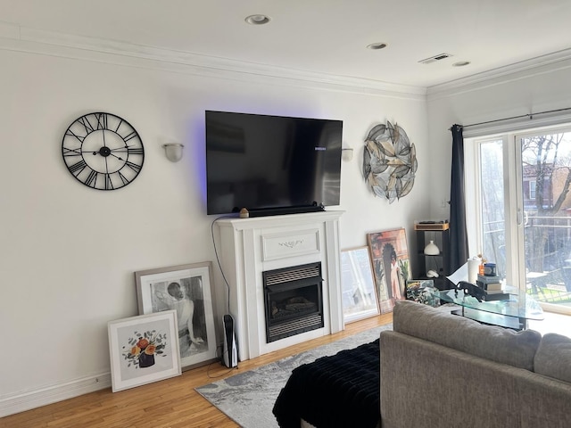 living room with baseboards, visible vents, a glass covered fireplace, crown molding, and light wood-type flooring