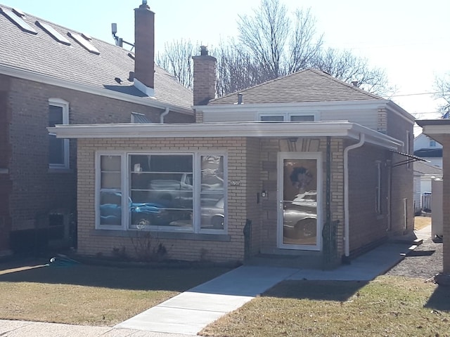 exterior space with a front lawn, brick siding, a chimney, and a shingled roof