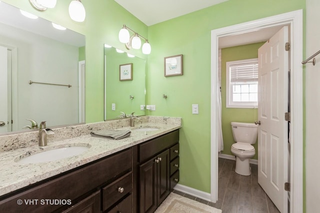 full bath featuring double vanity, toilet, baseboards, and a sink