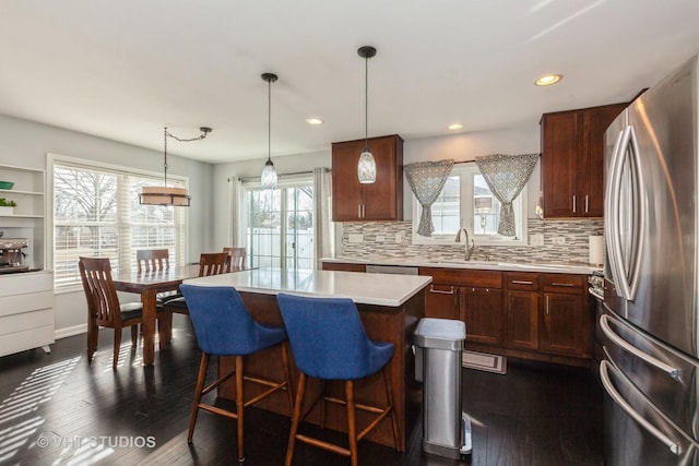 kitchen featuring freestanding refrigerator, a sink, light countertops, a kitchen bar, and a center island