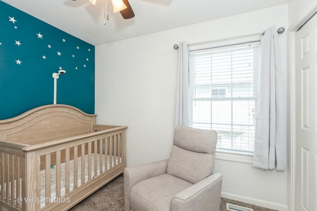 carpeted bedroom featuring a nursery area, baseboards, visible vents, and ceiling fan