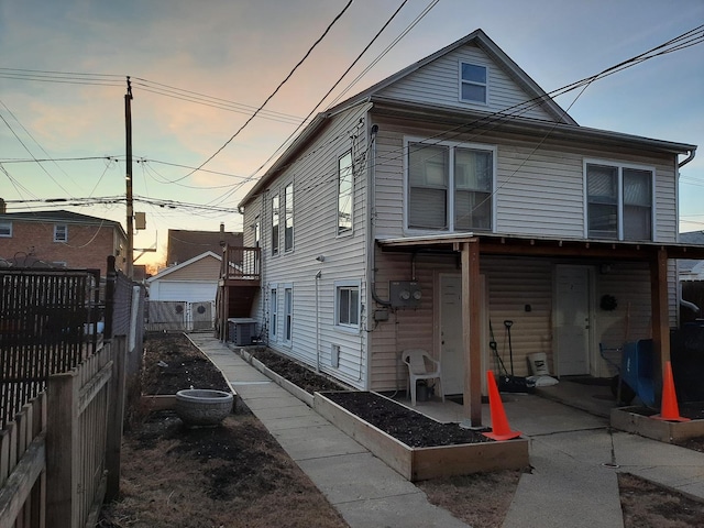 back of property at dusk with central air condition unit and fence