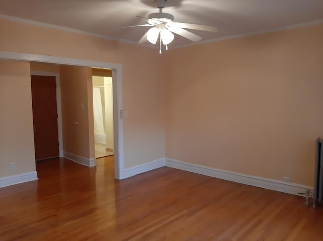 empty room with wood finished floors, baseboards, and ornamental molding