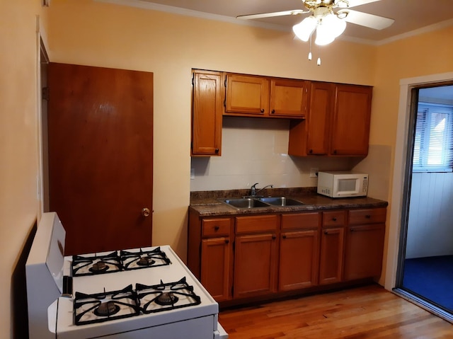 kitchen with dark countertops, crown molding, brown cabinets, white appliances, and a sink