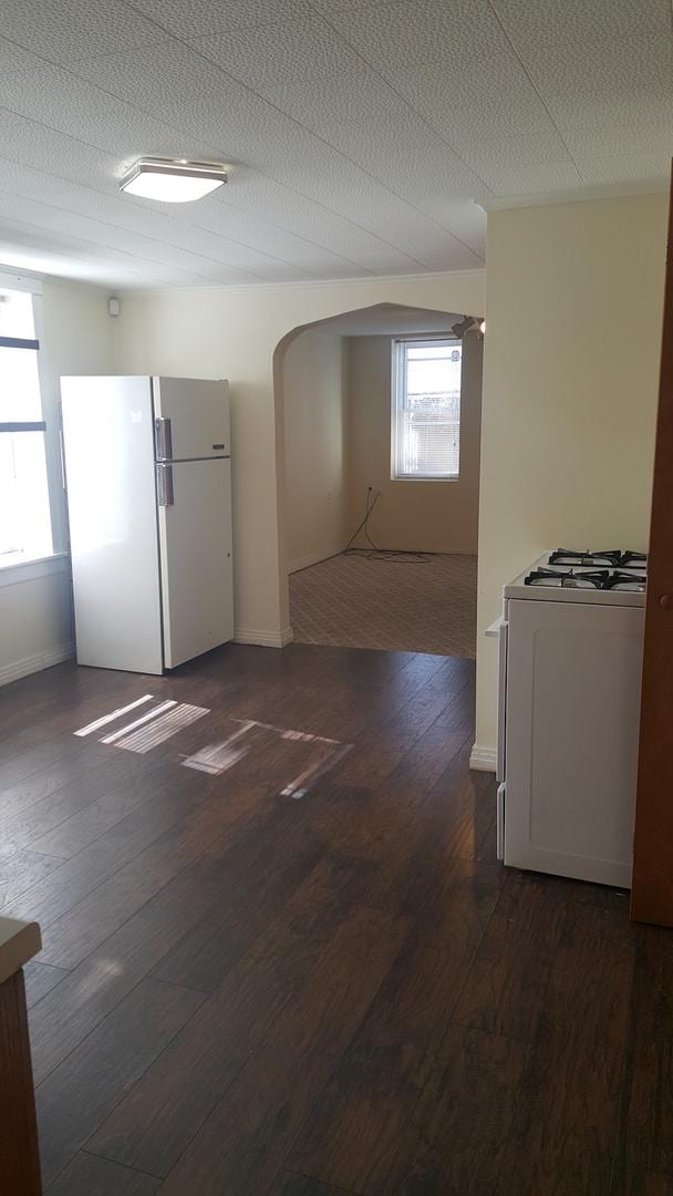 empty room with baseboards, arched walkways, wood-type flooring, and a textured ceiling