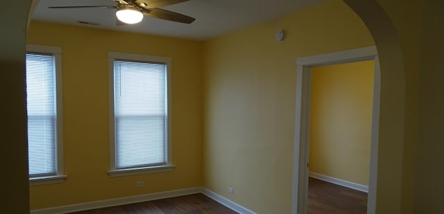 empty room with arched walkways, dark wood-style floors, baseboards, and ceiling fan