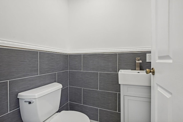 half bath featuring vanity, tile walls, toilet, and wainscoting