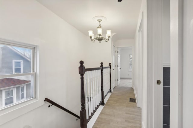 hall featuring baseboards, visible vents, a notable chandelier, an upstairs landing, and light wood-type flooring