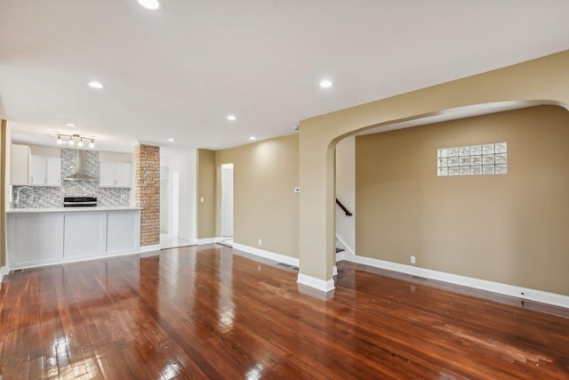 unfurnished living room featuring hardwood / wood-style flooring, recessed lighting, arched walkways, baseboards, and stairs