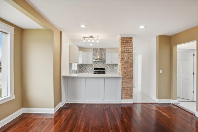 kitchen with wall chimney range hood, light countertops, decorative backsplash, stove, and ornate columns