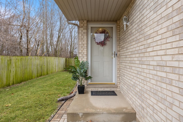 property entrance with a yard, brick siding, and fence