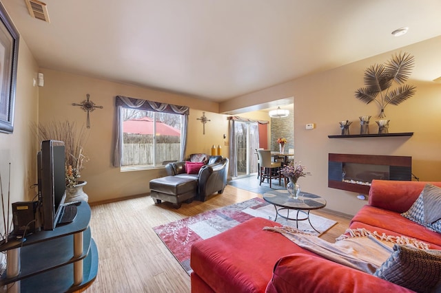 living area featuring a glass covered fireplace, wood finished floors, visible vents, and baseboards