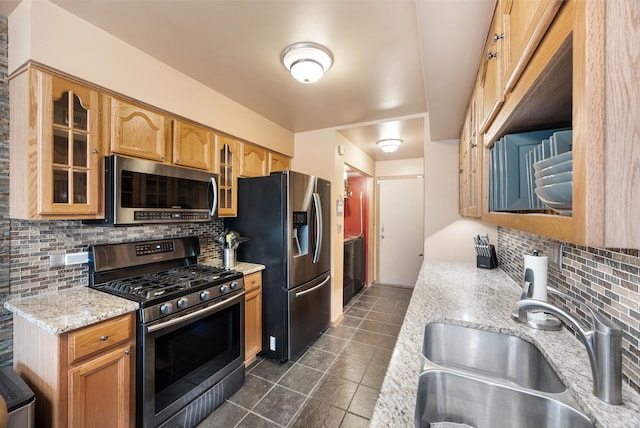 kitchen featuring tasteful backsplash, glass insert cabinets, light stone countertops, appliances with stainless steel finishes, and a sink