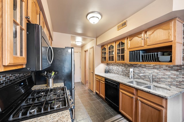 kitchen with light stone countertops, visible vents, a sink, black appliances, and glass insert cabinets