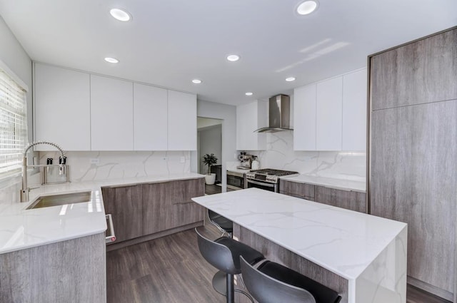 kitchen with stainless steel gas range oven, light stone counters, modern cabinets, wall chimney exhaust hood, and a sink