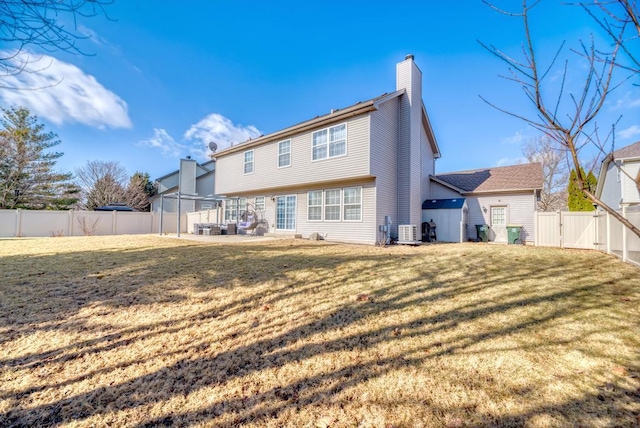 back of property with central AC, a lawn, a chimney, a fenced backyard, and a gate