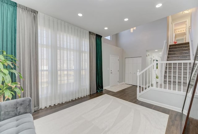 foyer entrance with wood finished floors, baseboards, recessed lighting, stairs, and a towering ceiling