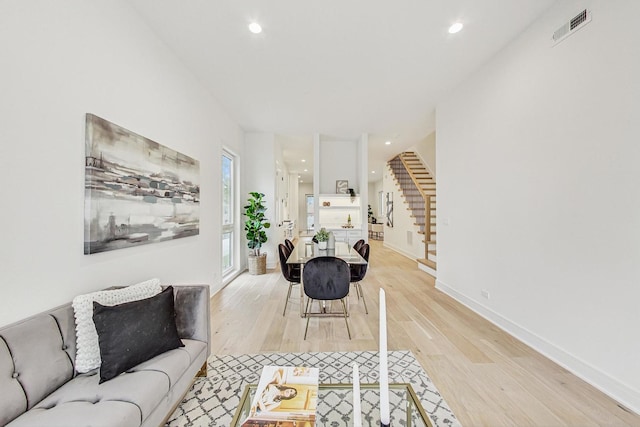 living area featuring light wood-type flooring, visible vents, baseboards, and stairway