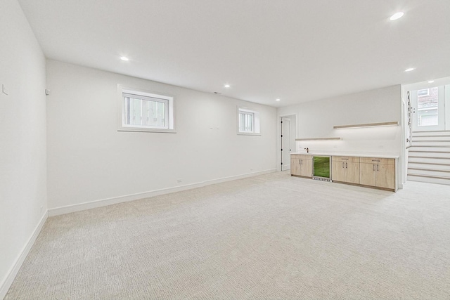 below grade area with beverage cooler, stairway, light colored carpet, and baseboards