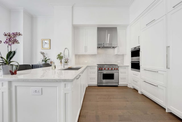 kitchen with crown molding, wall chimney range hood, appliances with stainless steel finishes, a peninsula, and a sink