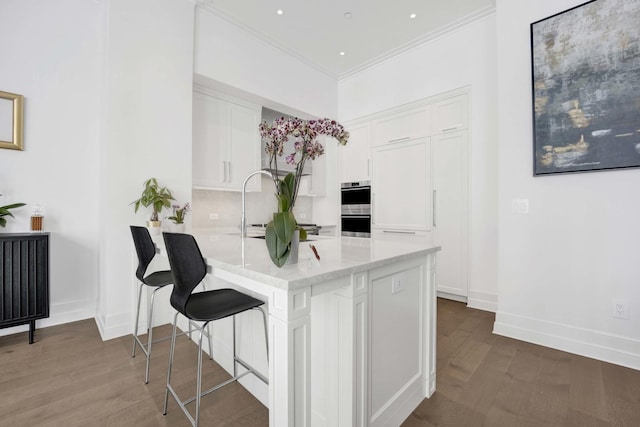 kitchen with wood finished floors, a peninsula, ornamental molding, white cabinetry, and double oven