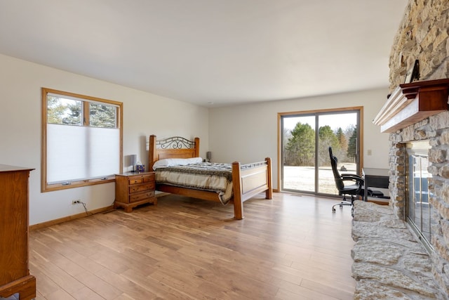 bedroom with baseboards, light wood finished floors, a stone fireplace, and access to outside