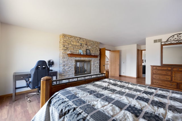 bedroom with a stone fireplace, baseboards, visible vents, and wood finished floors