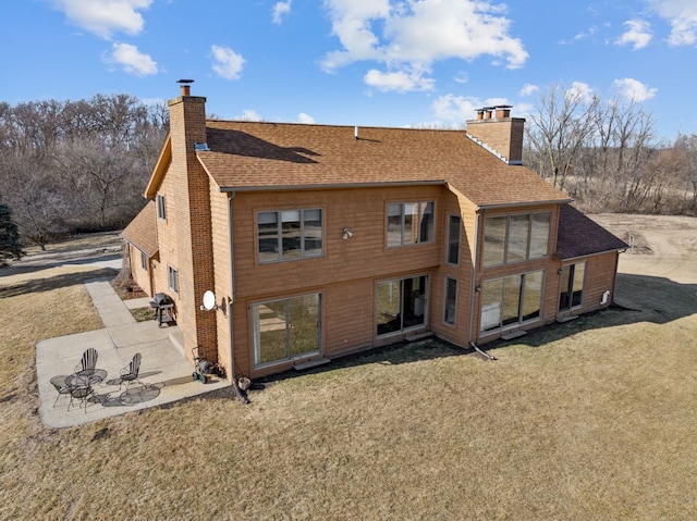 rear view of house with a patio area, a lawn, a chimney, and a shingled roof