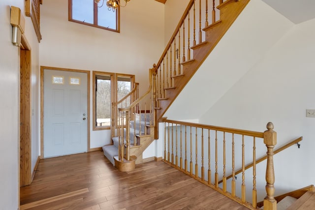 foyer entrance with a high ceiling, a notable chandelier, wood finished floors, and baseboards