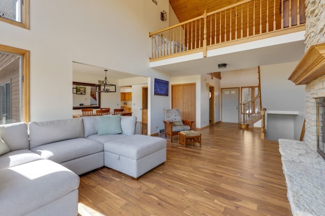 living area with light wood finished floors, a stone fireplace, stairs, and a towering ceiling