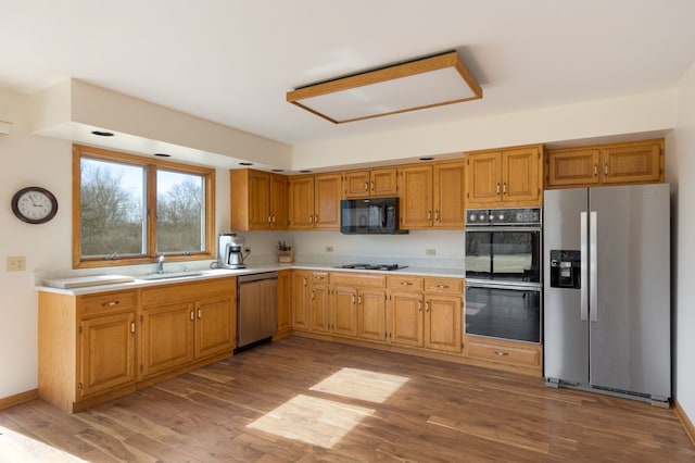 kitchen with light wood-type flooring, black appliances, light countertops, and a sink