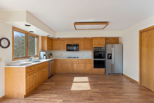 kitchen featuring light wood finished floors, baseboards, light countertops, black appliances, and a sink