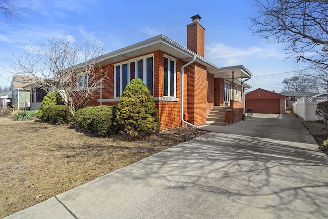 view of property exterior with an outbuilding, a chimney, brick siding, and fence