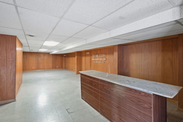 bar featuring light floors, wood walls, and a paneled ceiling