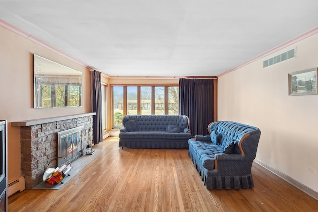 living room featuring visible vents, baseboards, ornamental molding, baseboard heating, and wood finished floors