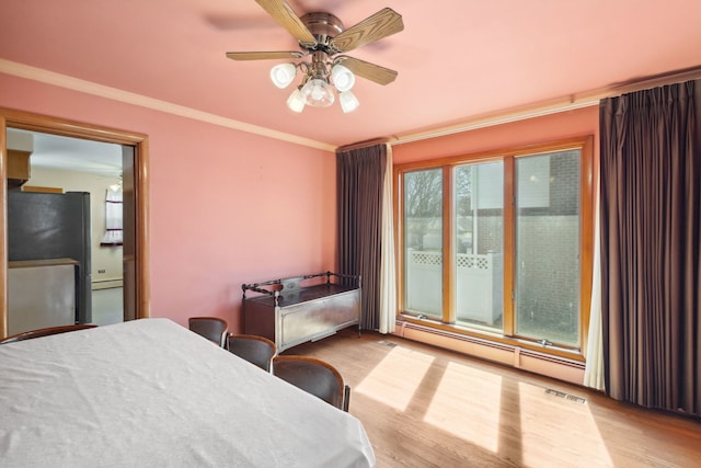 bedroom with wood finished floors, visible vents, a baseboard radiator, freestanding refrigerator, and ornamental molding