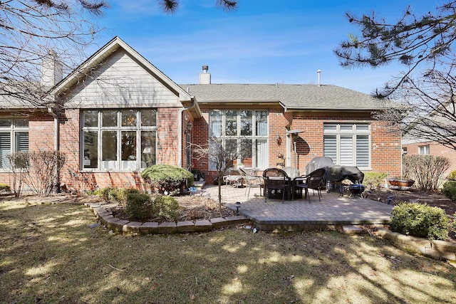 rear view of house featuring brick siding, a patio area, a chimney, and a lawn